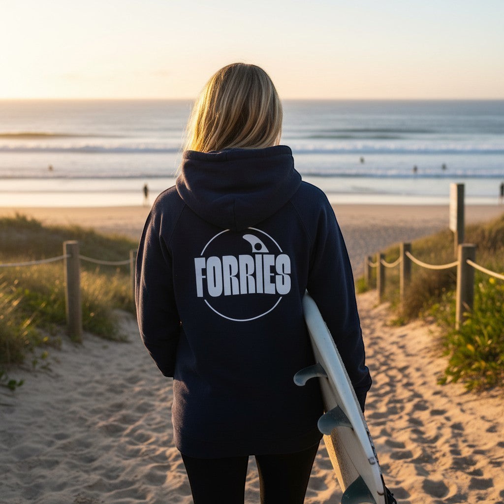 Sideliners unisex hoodie with Forries back print, worn by a woman holding a surfboard at the beach at sunset.