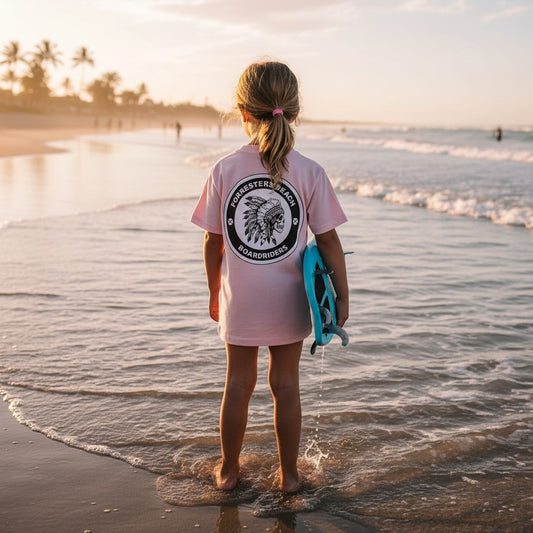 Sideliners light pink kid's t-shirt with Forresters Beach Boardriders back print, worn by a child on the beach.