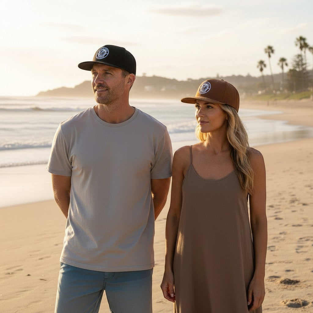 Sideliners trucker caps in black and brown worn by a man and woman on a sunny beach at sunset