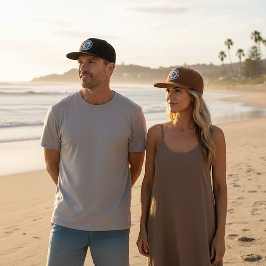 Sideliners trucker caps in black and brown worn by a man and woman on a sunny beach at sunset
