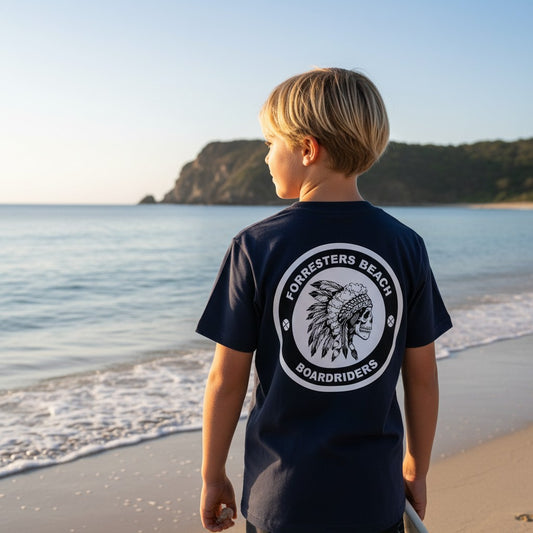 Sideliners youth navy cotton t-shirt with Forresters Beach Boardriders skull graphic on back, worn by boy at beach.